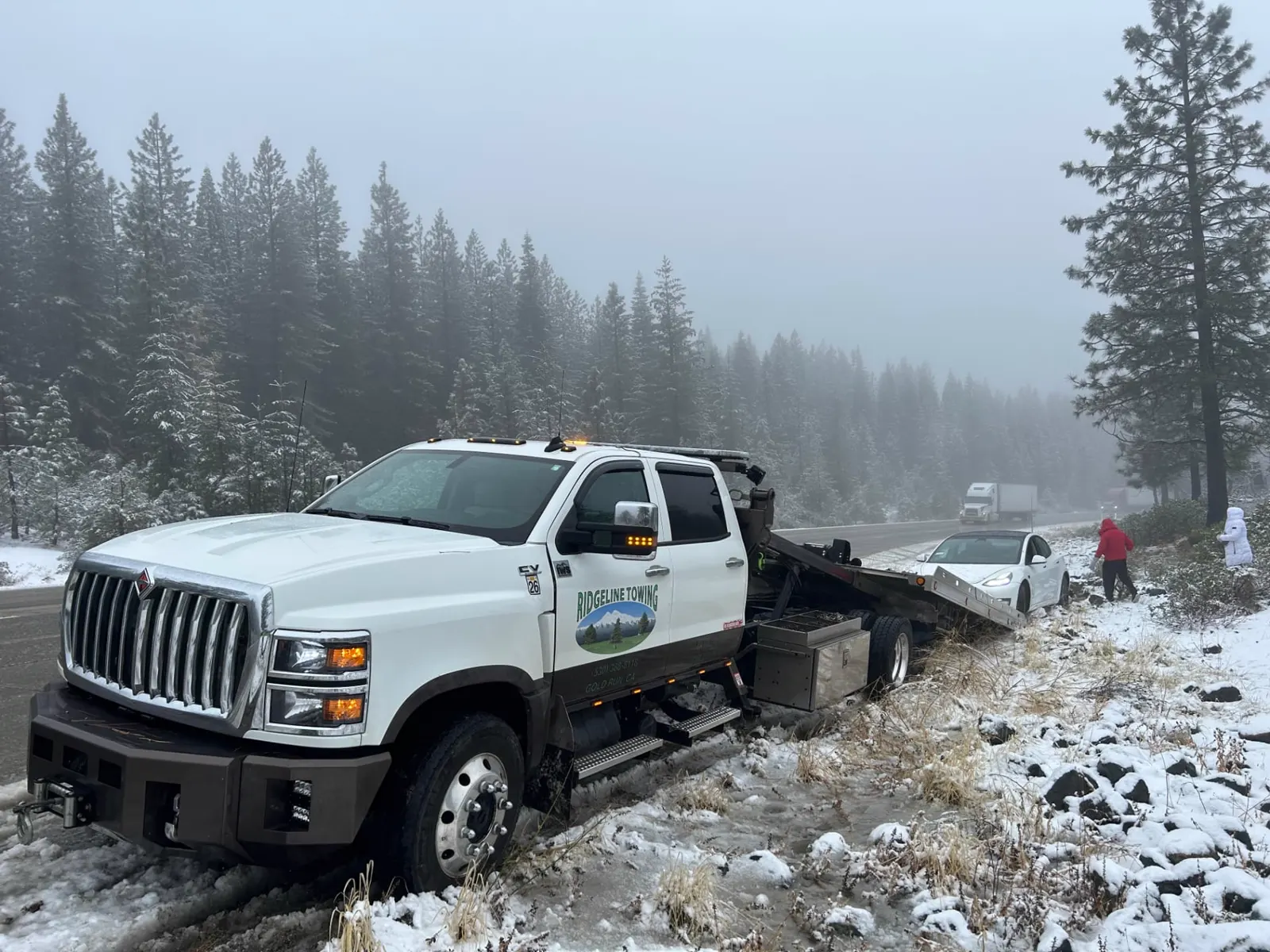 Ridgeline Towing flatbed recovering a car off an icy I-80 shoulder during a snowstorm