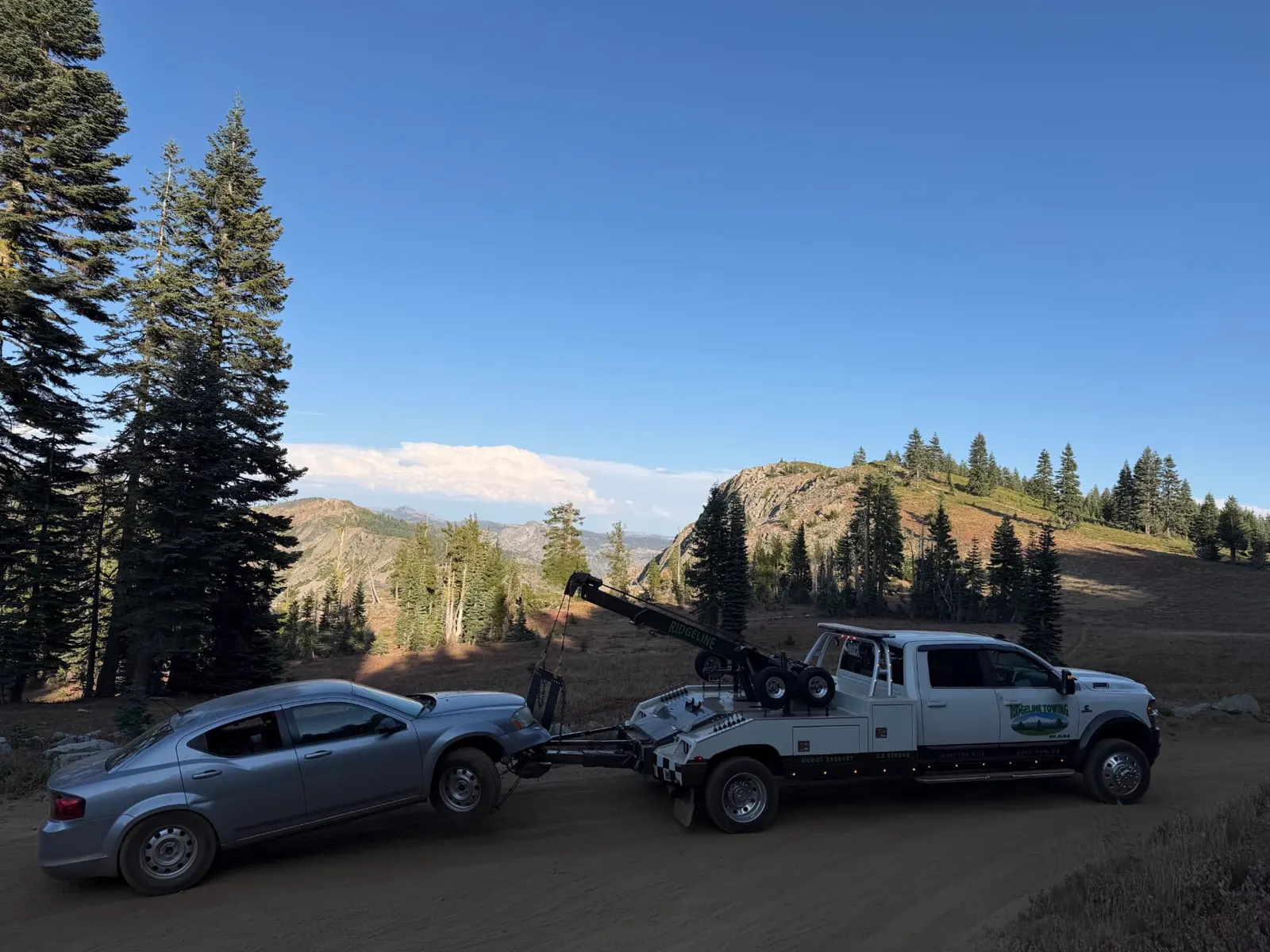 Ridgeline Towing wrecker towing a sedan off a high-country dirt road in the Sierra Nevada